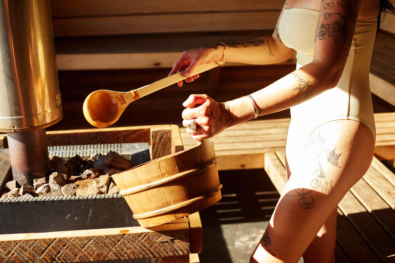Guest ladling water over the wood-fired stove inside the sauna